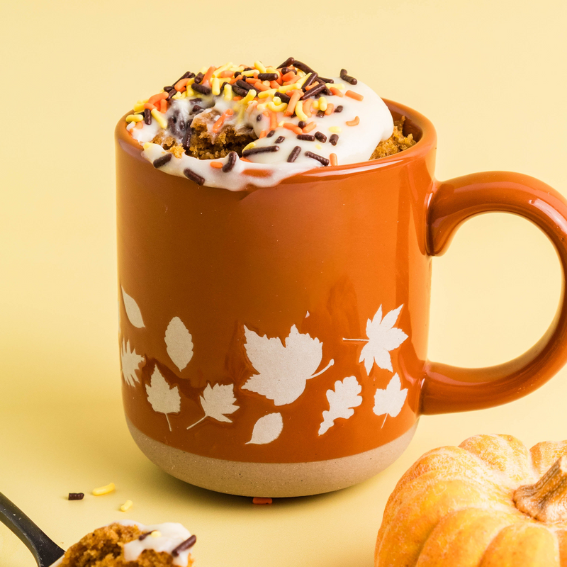Pumpkin spice mug cake with cream cheese frosting and autumn sprinkles in a terracotta leaf mug