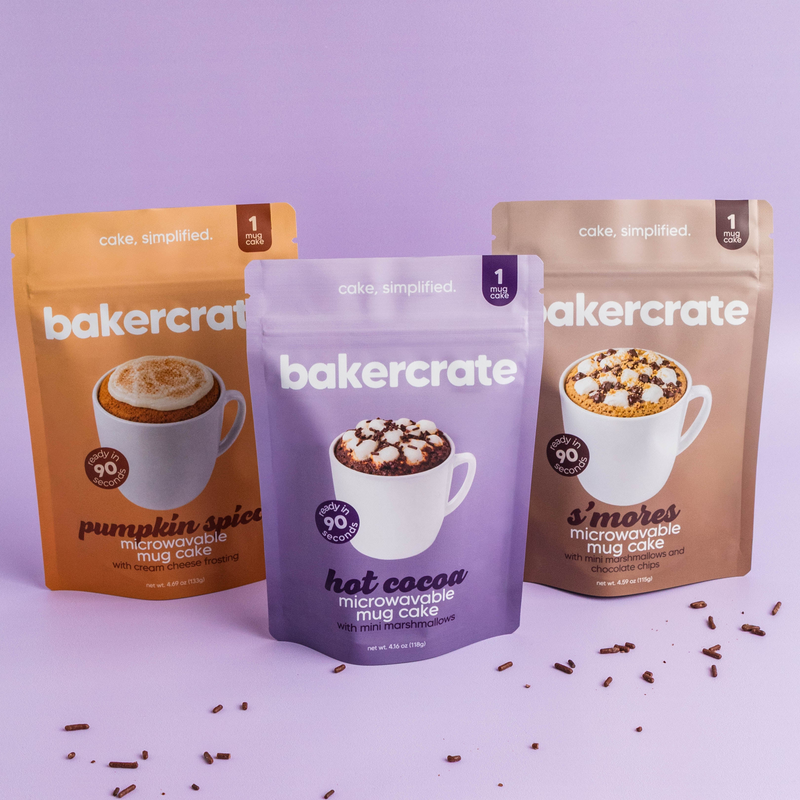 Three bakercrate mug cake pouches, pumpkin spice, hot cocoa and s'mores, on a lavender background with chocolate sprinkles