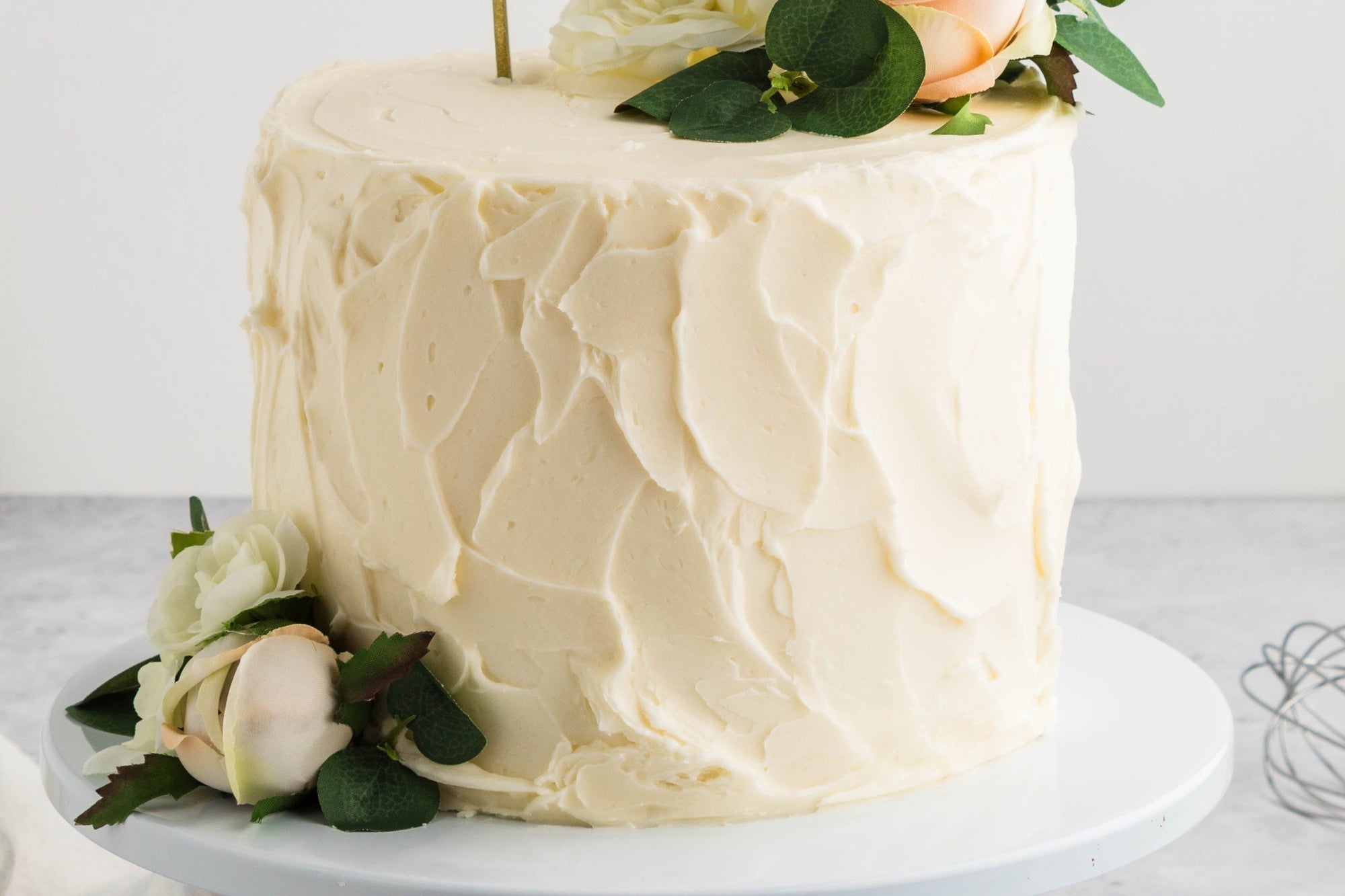 White cake with floral decorations and 'Oh Baby' topper on a light gray background