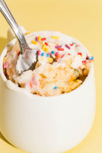 Close-up of a spoon lifting a bite of birthday cake mug cake on a yellow background