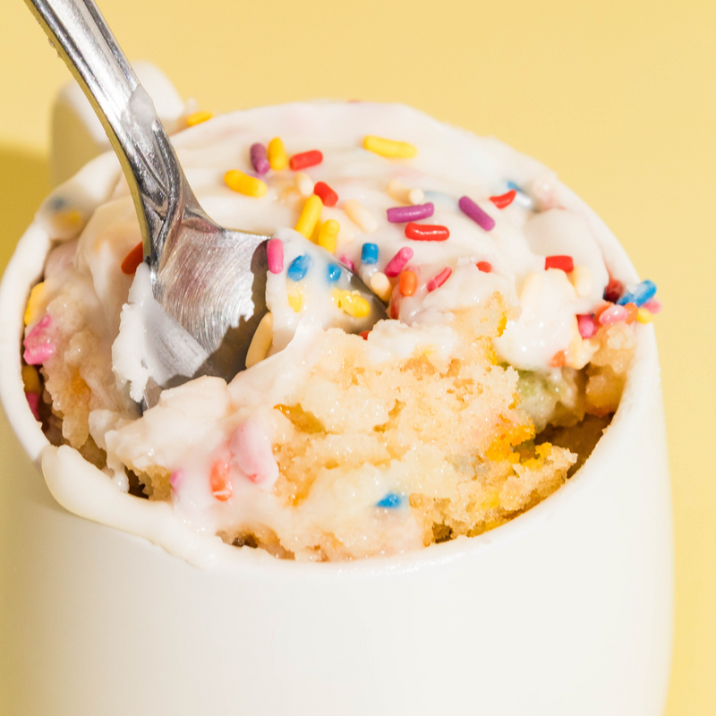 Close-up of a spoon lifting a bite of birthday cake mug cake on a yellow background