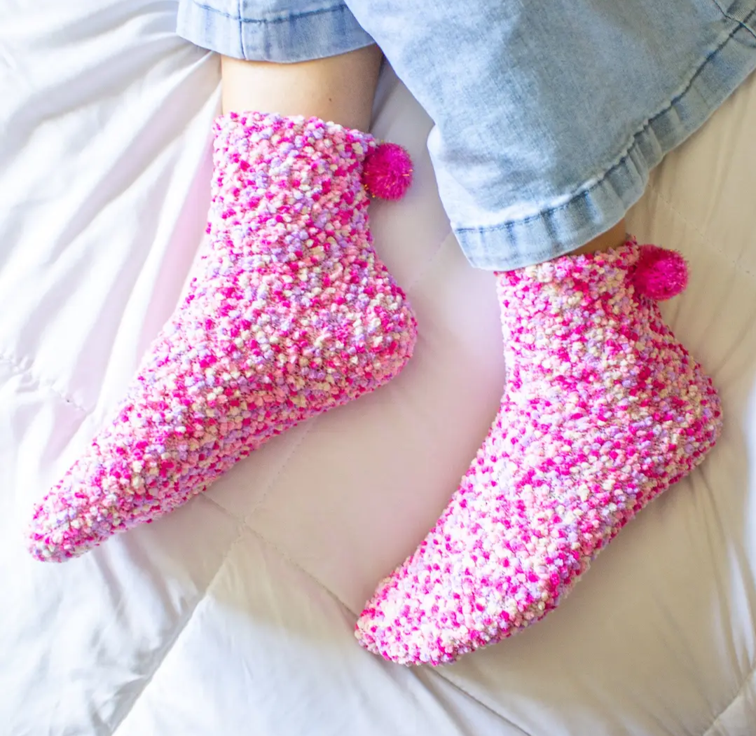 Fuzzy pink and white pom-pom socks worn with cropped jeans on a white quilt