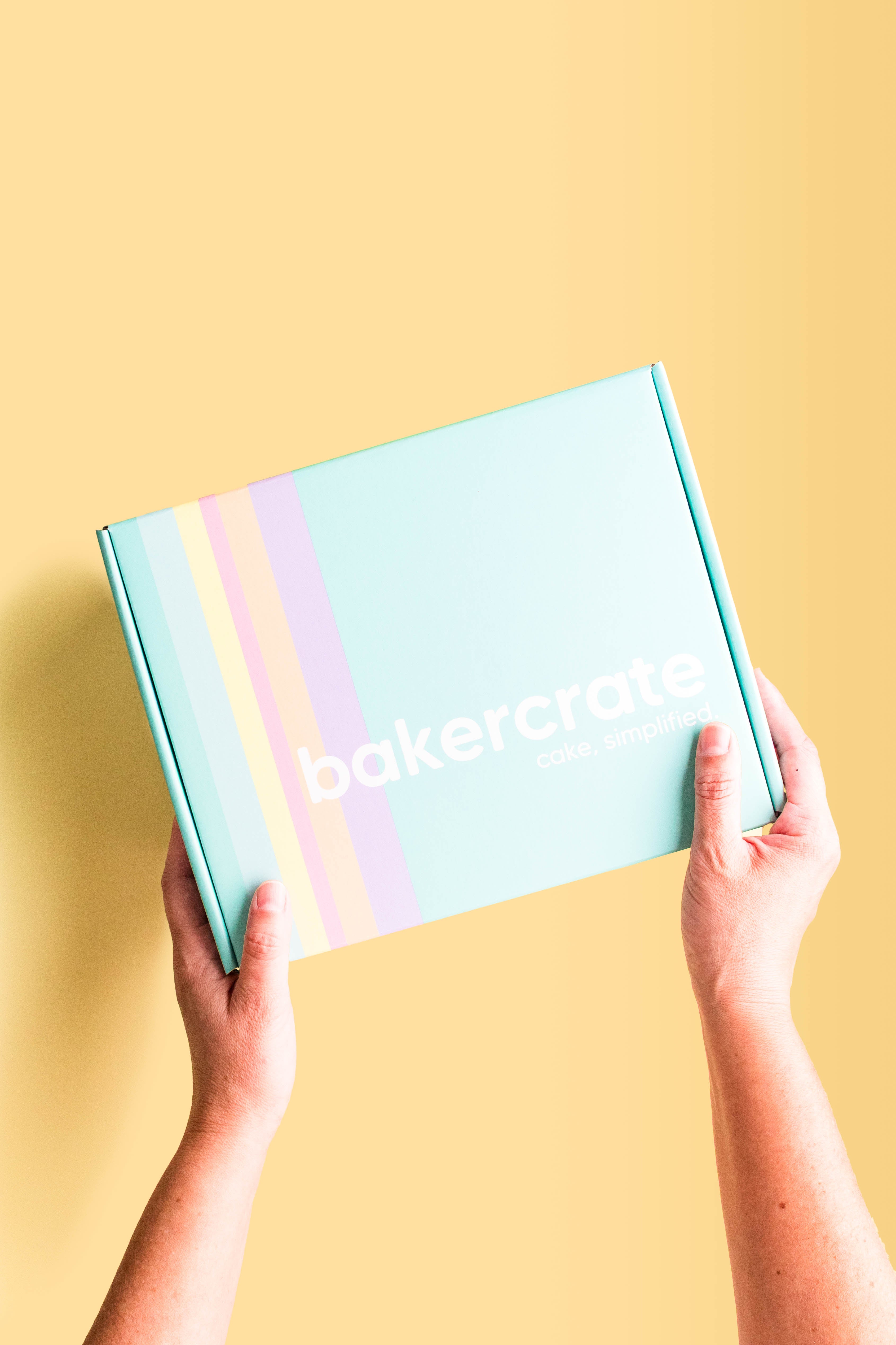 Hands holding a teal BakerCrate Birthday Mug Cake Kit shipping box