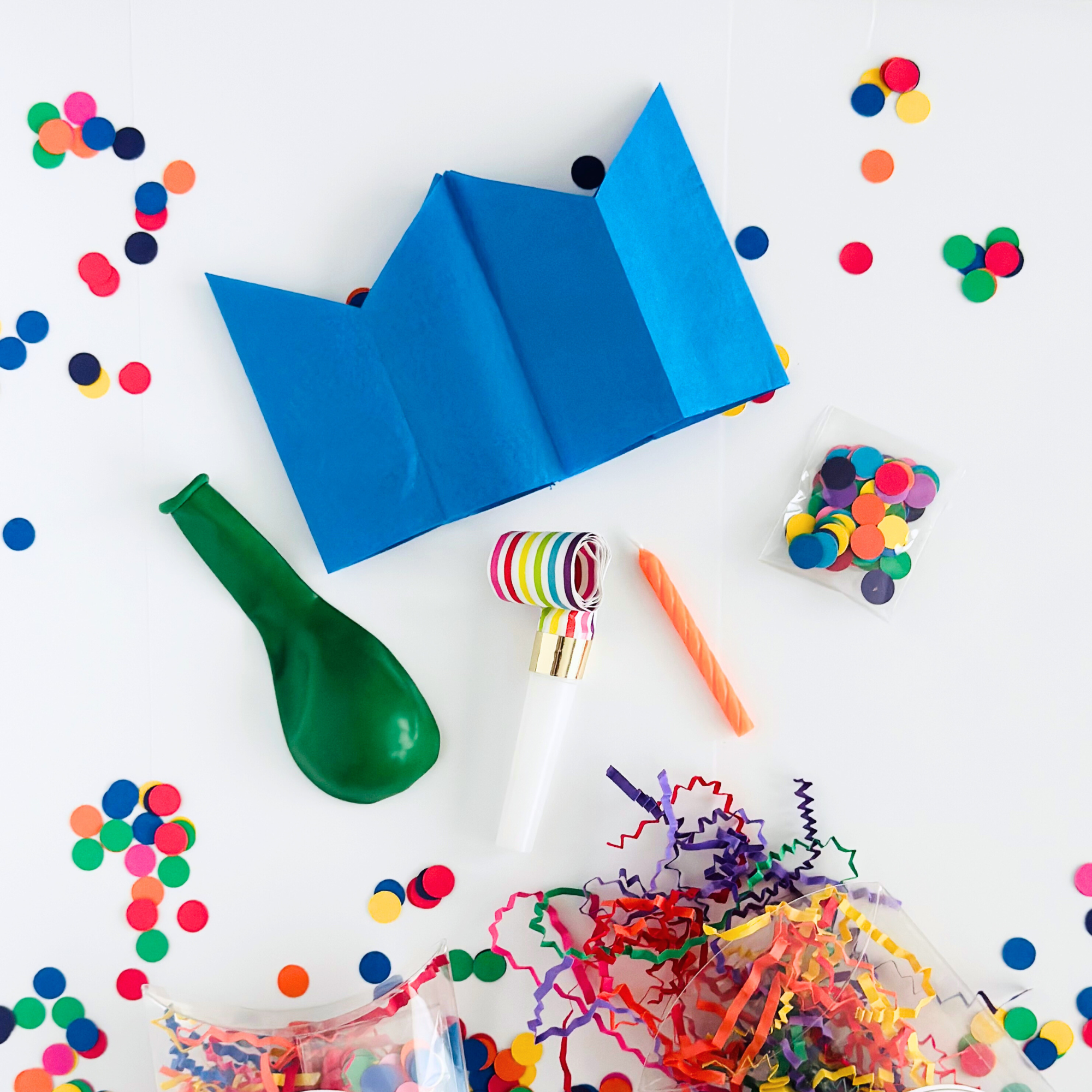 Celebration Kit contents laid out flat: blue paper crown, green balloon, striped party blower, orange candle, and bags of multicolored confetti and paper shred