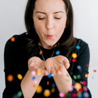Person blowing a handful of multicolored confetti toward the camera against a white background