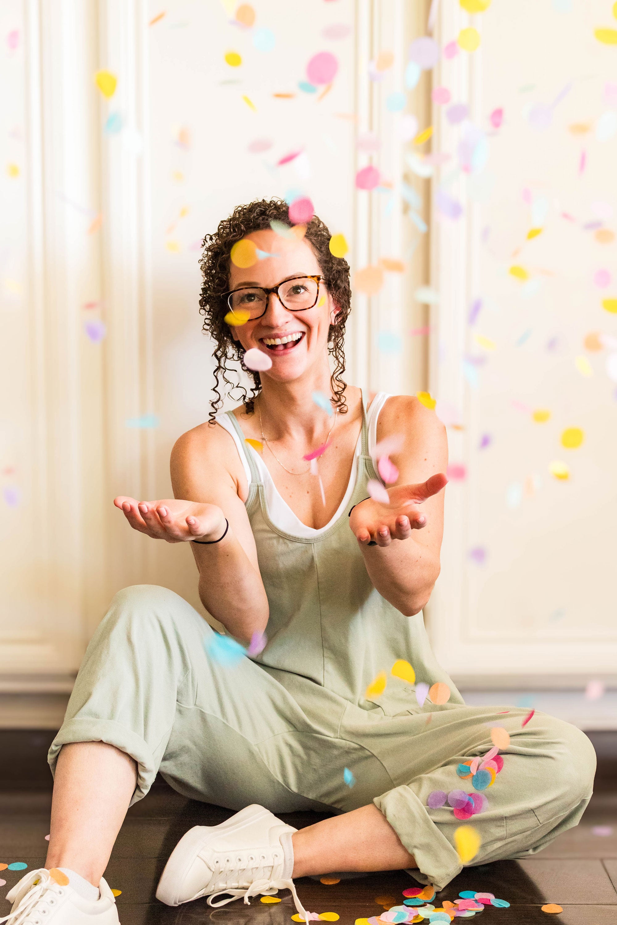 Maia sitting on the floor with colorful confetti around, wearing glasses and a light green outfit.