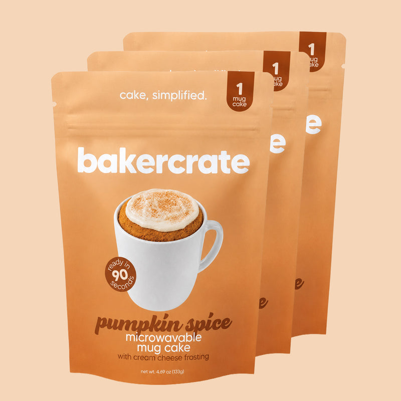 Three orange bakercrate pumpkin spice mug cake pouches on a peach background