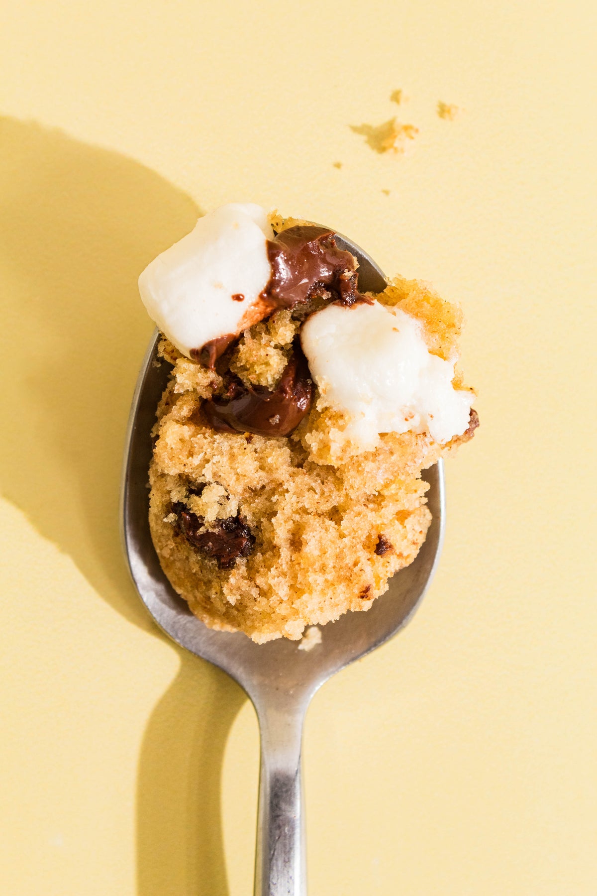 Close-up of a spoonful of s'mores mug cake with toasted marshmallow and melted chocolate on a yellow background