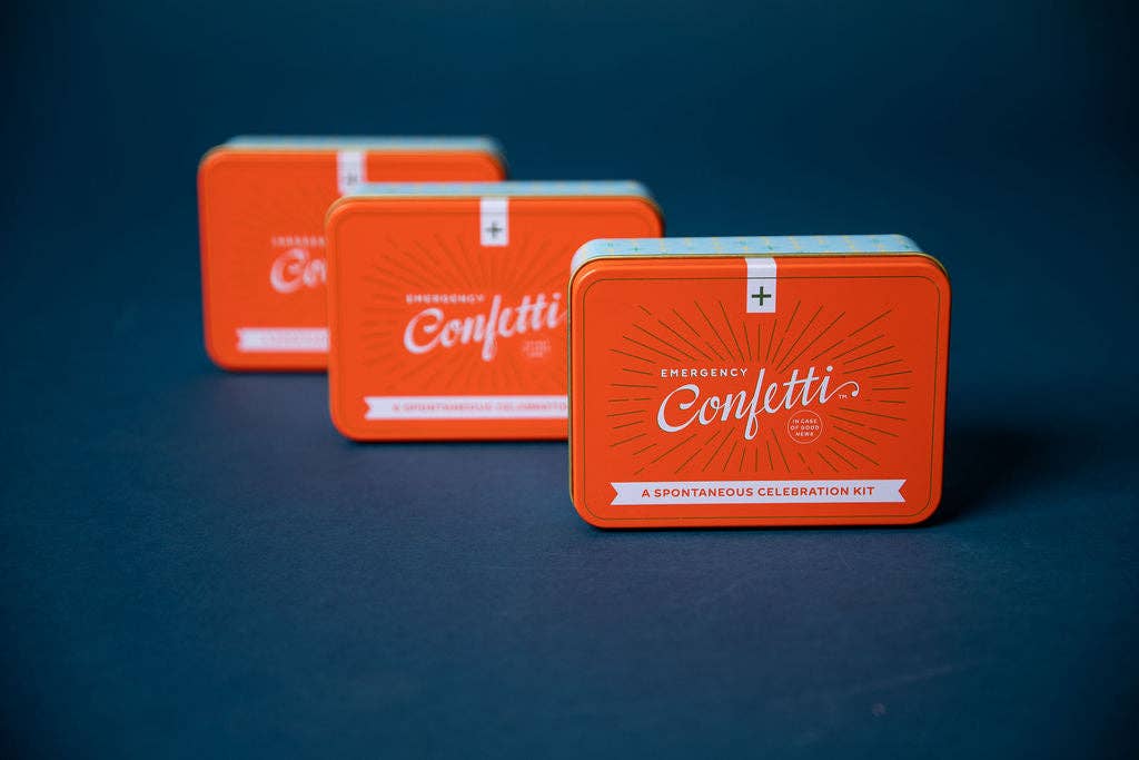 Three orange Emergency Confetti tins lined up in a row against a dark navy background