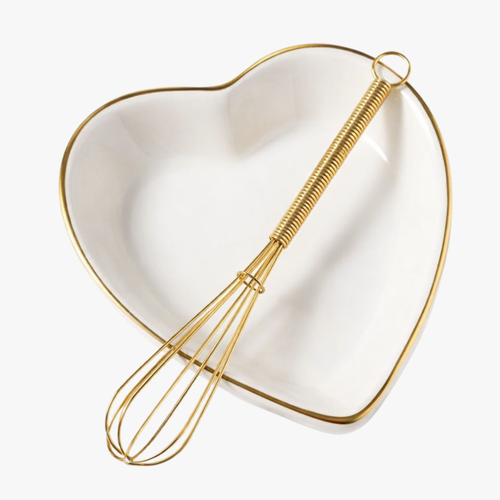 Gold mini wire whisk resting in a white heart-shaped ceramic dish
