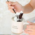 Person holding a spoon over a mug with dessert and 'Cozy Season' text.