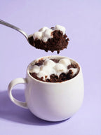 Hot cocoa mug cake with melted marshmallows in white mug, spoon lifting a bite on purple background