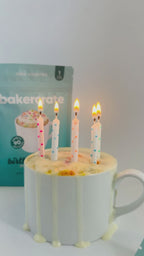 Birthday cake mug cake with dripping frosting and five lit candles beside a teal bakercrate birthday cake pouch