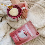 Hand holding a mug with a red velvet cake mix, surrounded by a textured beige blanket.