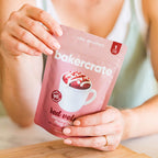 Hands holding a Bakercrate red velvet mug cake mix pouch on a cutting board