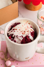 Red velvet mug cake with cream cheese frosting and pink sprinkles in a speckled mug
